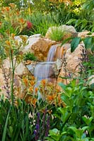 Detail of a sanstone waterfall made from rustic sandstone boulders, with a rockery style garden surrounding featuring a Anigozanthos 'Landscape Tangerine' and Viburnum odoratissimum 