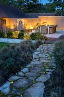 View up crazy paving path with embedded floor lighting to outside eating area in large Surrey Garden 