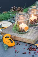 Scented candles made with spices, orange peel, pine and candles placed in jam jar on a wooden board