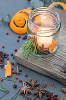 Scented candles made with spices, orange peel, pine and candles placed in jam jar on a wooden board