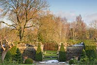 Clipped Buxus - Box - pyramids frame a gate leading from formal walled garden to an adjoining field with trees