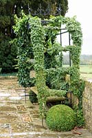 Hedera - Ivy - coated arbour with bench and topiary ball, on stone path
