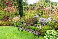 Packed border with Aster, ornamental grasses and Eupatorium, lawn and bench nearby