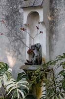 Small statue as wall fountain, surrounded by tropical foliage