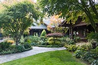 A paved path leads to the craftsman-style home, mixed beds of trees, conifers, shrubs, perennials and ornamental grasses 