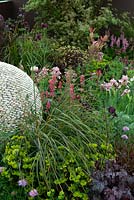 Herbaceous planting surrounding spherical feature made of pebbles in garden border - RHS Malvern Spring Festival 2014
