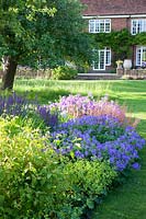 Summer bed with Geranium magnificum 'Rosemoor', Salvia, Heuchera and Alchemilla mollis, with lawn and house beyond. St Timothee, Berkshire, UK. 