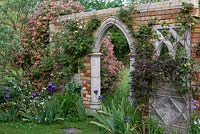 A folly from Redwood Stone lends support to clematis, climbing roses and early Dutch honeysuckle, Lonicera  periclymenum 'Belgica'.