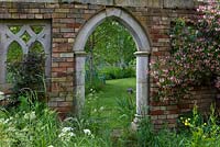 Framing a view of the garden beyond, a folly from Redwood Stone lends support to clematis, climbing roses and early Dutch honeysuckle, Lonicera  periclymenum 'Belgica'.