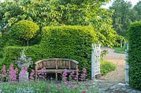 Topiary Taxus - Yew - hedge framing a garden bench and cast iron gates leading to gravel drive