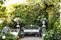 White ornate metal bench seats and urns on plinths, Courtyard garden, Italy.