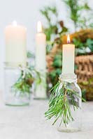 Candles in small glass bottles adorned with cut pine foliage