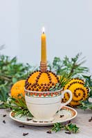 Orange studded with cloves in teacup holding a candle