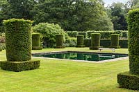 Clipped Yew columns - Taxus baccata - and reflective pool in the Silent Garden at Scampston Hall Walled Garden, North Yorkshire, UK. 