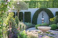 Contemporary Apothecary Garden with large water-basin surrounded by herb-lawn of Thymus serpyllum - Thyme. Umbrella-pruned Cratageus - Hawthorn, Myrtus communis - Myrtle. Taxus baccata - Yew topiary around sculpture of Aesclepius' staff, the symbol of healing. Rosa - Rose and Laurus nobilis - Bay