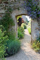 Stone arch in wall through to separate garden along a gravel path