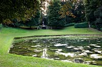 Pond set in lawn, behind stone bridge in sloped earthwork with classic statue  