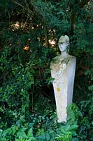 Stone statue amongst evergreens Taxus - Yew - and Ilex - Holly