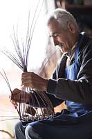 Experienced basket maker building a hand-woven basket on his knee. 
