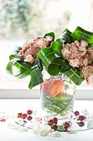 Contemporary floral bouquets displayed in vase, with curled Aspidistra leaves. 