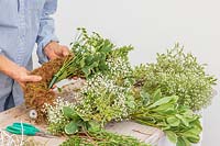 Woman fixing Chrysanthemum in floral water tube to moss wreath form. 