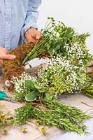 Woman fixing Chrysanthemum in floral water tube to moss wreath form.
