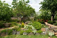A garden terrace, with a wall made of large pieces of blue stone planted with a variety of hardy shrubs and plants.