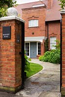 Entrance to house through black painted gate, curved paved path to front door, boundary brick wall matches house bricks