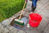 Cleaning a patio using a long-handled brush, water and vinegar