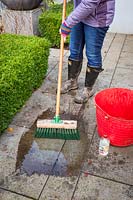 Cleaning a patio using a long-handled brush, water and vinegar