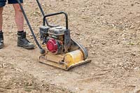 Man using petrol driven wacker plate to compact base for patio