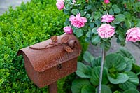 Still life consisting of rusty letterbox with rusty rose next to Rosa - Rose - grown as a standard