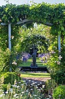 View through a Wisteria-covered pergola to a rectangular pond with sculpture