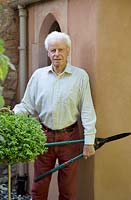 Man holding long-handled shears, standing by topiary