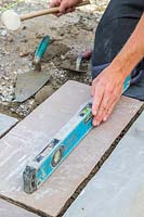 Man using a spirit level to check the level of freshly laid paving slabs