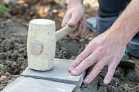 Man using rubber mallet to  level freshly laid sandstone setts
