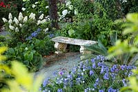 Stone bench in front of mixed bed with Hydrangea quercifolia, Bergenia and Agapanthus and Cycas revoluta