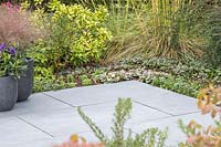 Slate patio with pot plants surrounded by bed with mixed planting