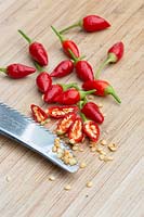 Whole and cut open Birds Eye Chillies with scraped out seeds and pith on a timber chopping board.