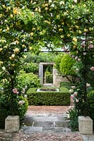 Archway in rose garden with view through to hedging and wall boundary with open doorway.