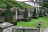 Line of topiary on lawn with wall behind, clipped pyramids within squares alternating with columns 