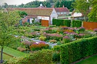 Overview of modern formal country garden, flower beds in blocks surrounded by hedges with view of buildings beyond