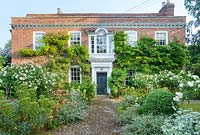 Docwra's Manor House with cobble path, standard roses alstroemerias and euphorbias.