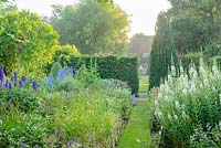 View towards house across walled garden with narrow grass path and wide range of herbaceous perennials including: Chamaenerion angustifolium 'Album' - White Rosebay Willowherb and Delphinium