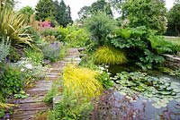 Natural pond with aquatic and marginal planting, to one side a deck boardwalk with mixed border