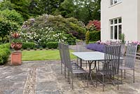 Table and chairs set up on terrace, surrounded by flowering borders.
