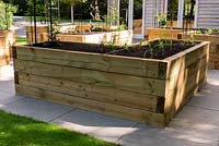 Raised vegetable beds made from modern wooden sleepers, on paved surface