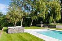 Modern garden with swimming pool and trees planted in raised beds edged with granite walls