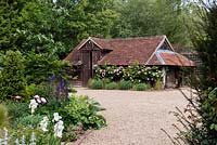 View over the gravel driveway to large outbuilding with Rosa - Climbing Rose