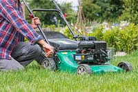 Woman adjusting the cutting height of a rotary lawn mower in long grass
